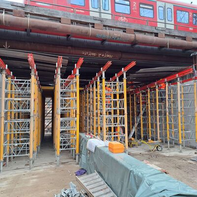 Schalungs- und Bewehrungsarbeiten an der Eisenbahnbrücke an der Golfstraße. Über die Brücke fährt oben ein Zug.
