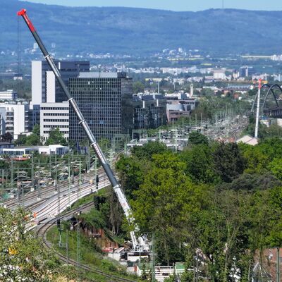Blick auf die Gleise. Ein Kran führt Arbeiten durch. Im Hintergrund ist eine Stadt.