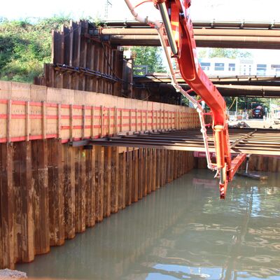 Ein Kran hebt einzelne Stäbe zwischen Stützwände. Darunter Wasser