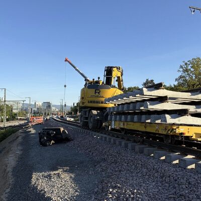 Ein gelbes Baufahrzeug auf Schienen liefert Gleise an.