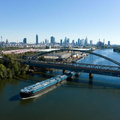 Ein blaues Schiff fährt unter einer Eisenbahnbrücke.
