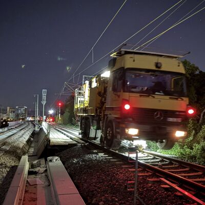 Ein gelbes Baufahrzeug steht in der Nacht auf den Gleisen.